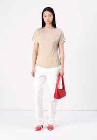 Haut beige à manches courtes associé à un pantalon blanc. Sac à main rouge de forme courbe et chaussures à talons rouges avec des accents argentés.
