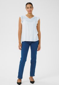 Blouse bleu clair avec des manches à volants et un décolleté en V, assortie à un jean slim fit bleu marine et des chaussures noires à bout pointu. Design simple, texture lisse.