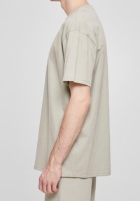 Jasnoszara bawełniana koszulka z krótkim rękawem, luźny krój, okrągły dekolt oraz widoczne szwy na rękawach i dolnym brzegu. Prosty design.