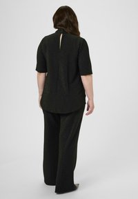Zwarte metallic top met korte mouwen, hoge kraag en een sleuteltje aan de achterkant. Gecombineerd met losse zwarte broeken. Soepele textuur.