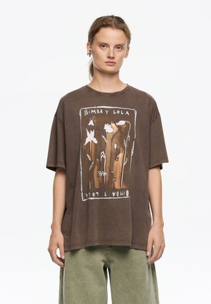 Brązowy, oversize T-shirt z grafiką z przodu, przedstawiającą kwiaty i liście, nadrukowaną w jasnych odcieniach. Wykonany z miękkiej bawełny, z krótkimi rękawami.