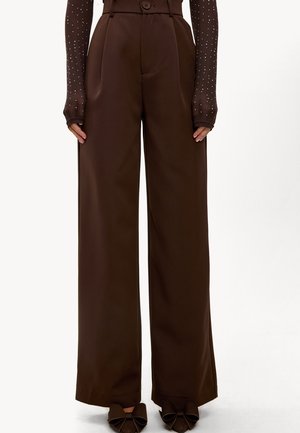 Hoge taille brede bruine broek met knoopsluiting, gecombineerd met doorzichtige lange mouwen versierd met kleine witte stippen en bruine strik schoenen.