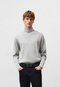 Szary sweter z golfem o prążkowanej fakturze, z długimi rękawami i kołnierzem średnio-wysokim, zestawiony z czarnymi spodniami i paskiem.