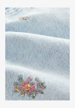 Helles blaues Denim-Gewebe mit einer strukturierten Webart, das am Rand mit floralen Stickereien in Pink, Gelb und Grün verziert ist.