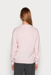 Jasnoróżowy sweter wykonany z miękkiego materiału, z luźnym krojem, długimi rękawami i prostym dekoltem typu crew neck, w połączeniu z pasiastymi spodniami.