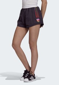 Černé šortky s texturovaným povrchem, zdobené duhovými pruhy a květinovým logem na lemu. Kombinované s černobílými teniskami.