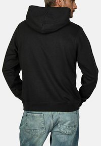 Zwarte shirt met capuchon van zacht materiaal, voorzien van een kangoeroezak, geribde manchetten en een platte koord voor de capuchon. Achteraanzicht weergegeven.