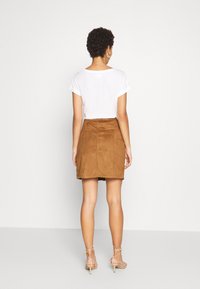 Brun mockaskinns minikjol med figurnära midja och bakfickor, ihopparad med en enkel vit t-shirt och nude remsandaler.