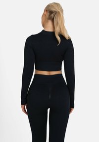 Čierny rebrovaný dlhý rukáv cropped top s priliehajúcim strihom, skombinovaný s legínami s vysokým pásom. Štruktúra vyzerá elasticky a tesne prilieha.