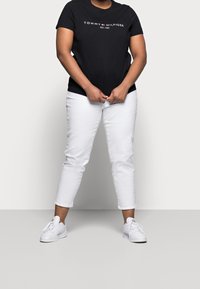 Sort t-shirt med korte ærmer med "Tommy Hilfiger" logo i hvid og rød, parret med hvide cropped bukser og hvide sneakers. Simpelt, afslappet outfit.