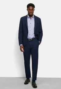 Navy suit with tailored jacket and matching trousers, paired with a light purple button-up shirt. Features a black belt and polished black shoes.