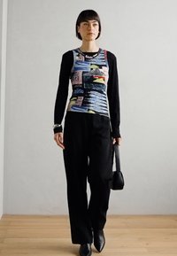 Multicolored patterned long-sleeve top with a fitted shape, paired with black wide-leg trousers and sleek ankle boots, held black bag.