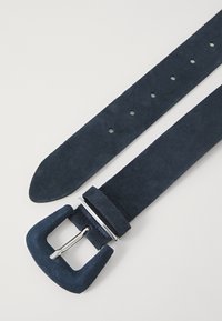 Cintura in suede blu navy con forma piatta, dotata di una fibbia rettangolare in argento e diversi fori per la regolazione della taglia. Texture morbida in tutto il suo sviluppo.