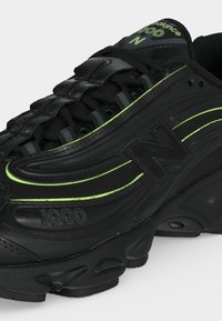 Baskets New Balance 1000 noires avec des accents vert fluo et des lacets noirs sur fond blanc.