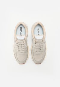 Beige sportschoenen gemaakt van mesh en synthetische materialen; voorzien van witte veters, lichtblauwe inlegzolen en gestructureerde zolen. Merkl logo is zichtbaar.