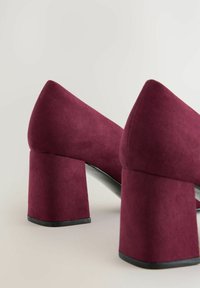Scarpe con tacco alto color bordeaux con finitura in suede testurizzato, dotate di ampi tacchi a blocco e punte appuntite. Le suole sono nere e leggermente lucide.