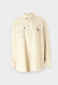 Beige skjorte med knappestolpe og spiss Krage, to brystlommer og trykknapper. Laget av et glatt stoff; har en liten logo-patch på venstre lomme.