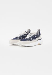 Sports shoes featuring a navy mesh upper with grey suede accents, thick white sole, and grey laces. Vibram logo on sole.