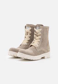 Botas de tobillo beige con lados perforados, acabado de ante texturizado, suelas de goma blanca y cordones crema, diseñadas para transpirabilidad y comodidad.