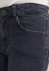 Mörka denimjeans med en åtsittande passform. Har en framficka, en knappstängning med en präglad logotyp, och sömmar med detaljer längs sömmarna.