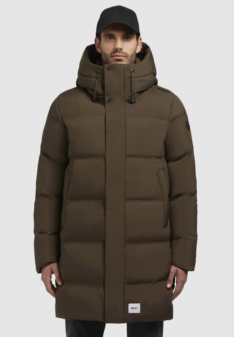 Manteau en duvet marron avec fermeture éclair à l'avant, capuche ajustable et grandes sections matelassées. Dispose de poches latérales et d'un patch logo sur l'ourlet.
