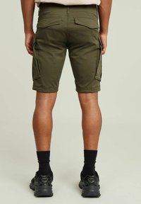 Pantaloni cargo verdi oliva con molte tasche laterali e taglio al ginocchio, realizzati in tessuto di cotone, con una cintura dotata di passanti per cintura.