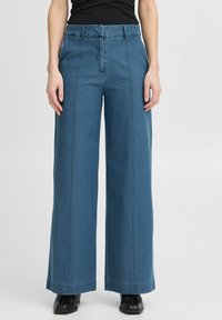 Brede denimbroek in een middelblauwe kleur, met een hoge taille, zichtbare stiksels en een soepele textuur. Vlakke voorkant met een middennaad.