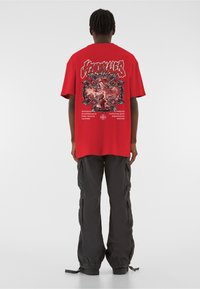 Punane graafiline T-särk, mille tagaküljel on keeruline musta ja valge kujundus. Sobib vabalt istuvate mustade cargo-pükstega, millel on mitmed taskud.