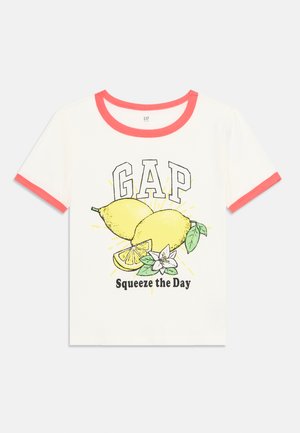 Balta T-kreklu ar korallkrāsas apdari, kurā attēlotas divas citrons, lapas un teksts "Squeeze the Day" melnā krāsā. Izgatavots no kokvilnas, ar īsām piedurknēm.