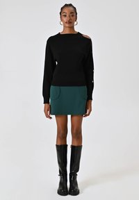 Maglione nero con spalla scoperta, abbinato a una mini gonna verde con due tasche frontali. Stivali neri trasparenti al ginocchio completano il look.