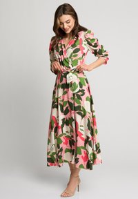 Kwiatowa sukienka o kroju w kształcie litery A w odcieniach różu, zieleni i bieli, z rękawami 3/4, z marszczeniem w talii i zwiewnym dołem. Materiał wydaje się gładki i lekki.