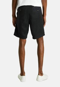 Shorts en coton noir avec une coupe décontractée, poches latérales et deux poches arrière, présentant une texture lisse et un ourlet roulé. Portés avec des chaussures blanches.