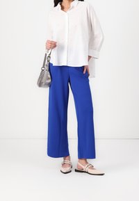 Biała koszula z długim rękawem z subtelnymi ozdobami, zestawiona z jasnoniebieskimi spodniami z szerokimi nogawkami i jasnoróżowymi wsuwanymi butami. Srebrna torebka.