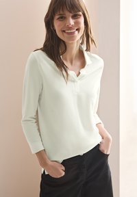 Lys grøn, langærmet polo skjorte med knapkrave. Blødt stof med en afslappet pasform, parret med sorte, højhalsede bukser.