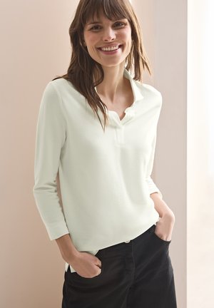 Polo shirt verde chiaro a maniche lunghe con colletto abbottonato. Tessuto morbido con una vestibilità comoda, abbinato a pantaloni neri a vita alta.