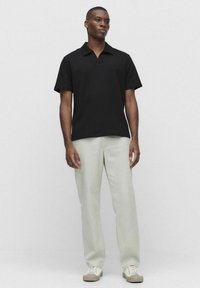 Svart kortärmad polo med texturerad tyg och krage, i kombination med ljusgröna byxor och beige sneakers. Enklare design.