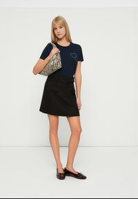 Camiseta de marinero con un diseño de corazón, mini falda negra con bolsillos y bolso estampado. Zapatos oscuros brillantes con detalle de lazo.