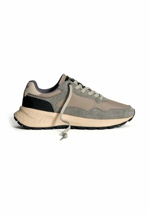 Lage sneaker in beige, grijs en zwart met een gestructureerde zool, vetersluiting en stoffen logo op de zijkant en de hiel.