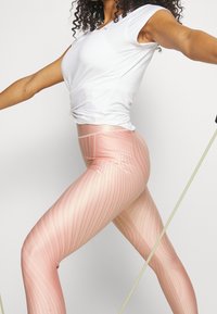Leggings sportivi rosa chiaro con strisce verticali, dotati di un alto elastico in vita e una texture liscia e elastica; abbinati a una maglietta bianca aderente.