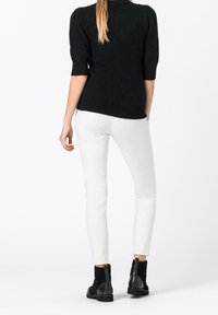 Maglione nero lavorato a maglia con maniche corte, pantaloni bianchi slim-fit e stivaletti neri alla caviglia con dettagli in suede texturizzato.