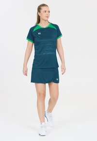 Tank top sport outfit i teal med korte ærmer, grønne detaljer og en matchende nederdel, lavet af letvægts, fugttransporterende stof.