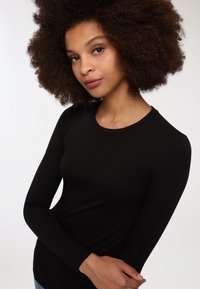Czarna bluzka z długim rękawem i okrągłym dekoltem, wykonana z miękkiego materiału. Posiada elegancki, dopasowany fason i gładką teksturę. Bez widocznych wzorów czy akcentów.