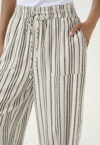 Pantalons larges rayés en beige et gris, dotés d'une taille à cordon et de poches latérales, fabriqués à partir d'un tissu léger et texturé.