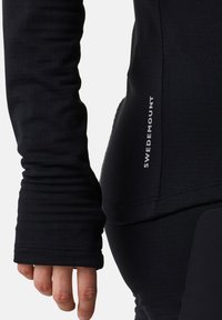 Svart långärmad topp med en figurnära design. Har tumhål, sömdetaljer och en liten vit "SWEDEMOUNT"-logotyp på sidan.