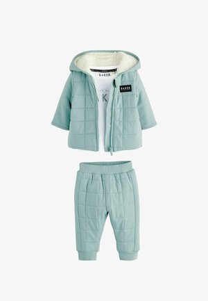 Világoskék steppelt babakapucnis pulóver műszőrme béléssel, elöl cipzárral, hozzáillő nadrággal, valamint egy logós fehér pólóval alatta.