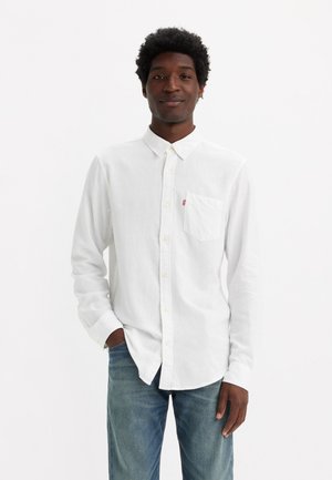 White long-sleeve shirt made of lightweight fabric with a buttoned collar, featuring a chest pocket and subtle texture. Paired with blue jeans.