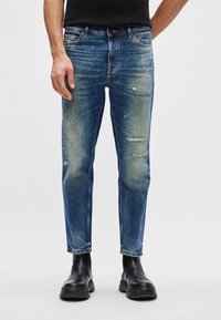Blå denim jeans med slim fit, som har slitte detaljer, falmet finish og mørk søm, kombinert med svarte ankelstøvler.