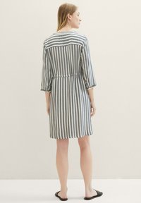 Robe rayée en gris et blanc, tissu léger, manches trois-quarts, taille cintrée, longueur genou, et un détail de pattes de boutonnage au dos.