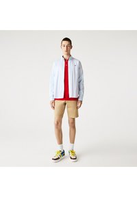 Light blue button-up shirt over a red polo, paired with tan shorts and multi-colored sneakers. Smooth fabric and casual design.