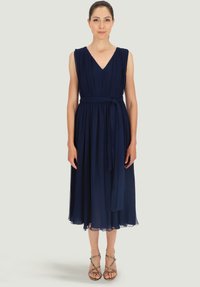 Granatowa, do kolan sukienka z dekoltem w kształcie litery V, plisowanym gorsetem i tkaninowym paskiem. Przezroczysty brzeg i miękka struktura, w połączeniu z sandałami na cienkich paskach.